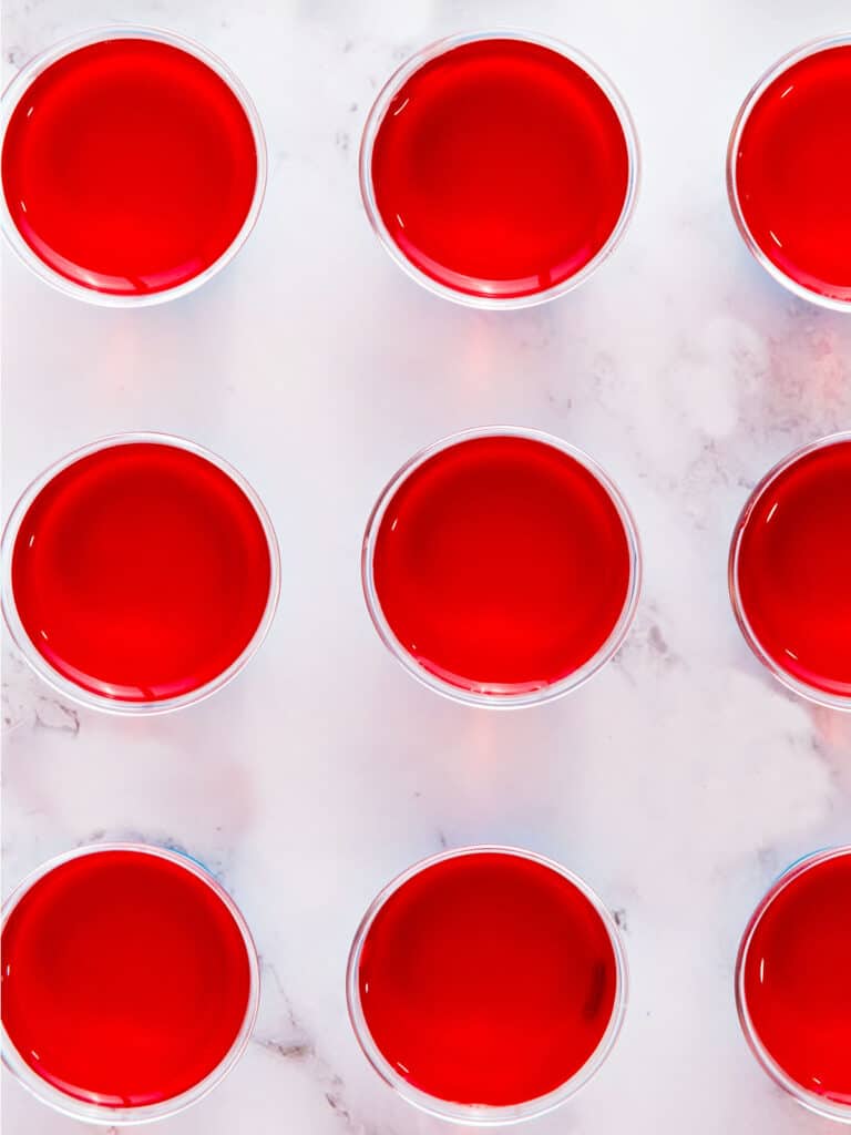 Marble background with rows of small plastic cups with red gelatin layer.