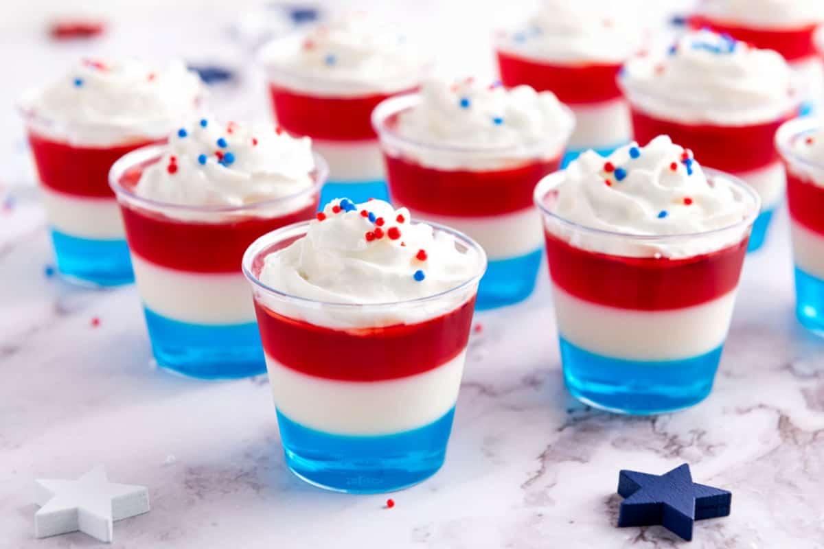 Cream topped patriotic jello cups on white marble.