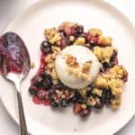 Close up serving of blueberry crumble on a white plate. Silver spoon.