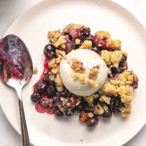 Close up serving of blueberry crumble on a white plate. Silver spoon.