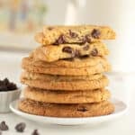 White background and plate with stack of chocolate chip cookies with raisins. Top one is halved.