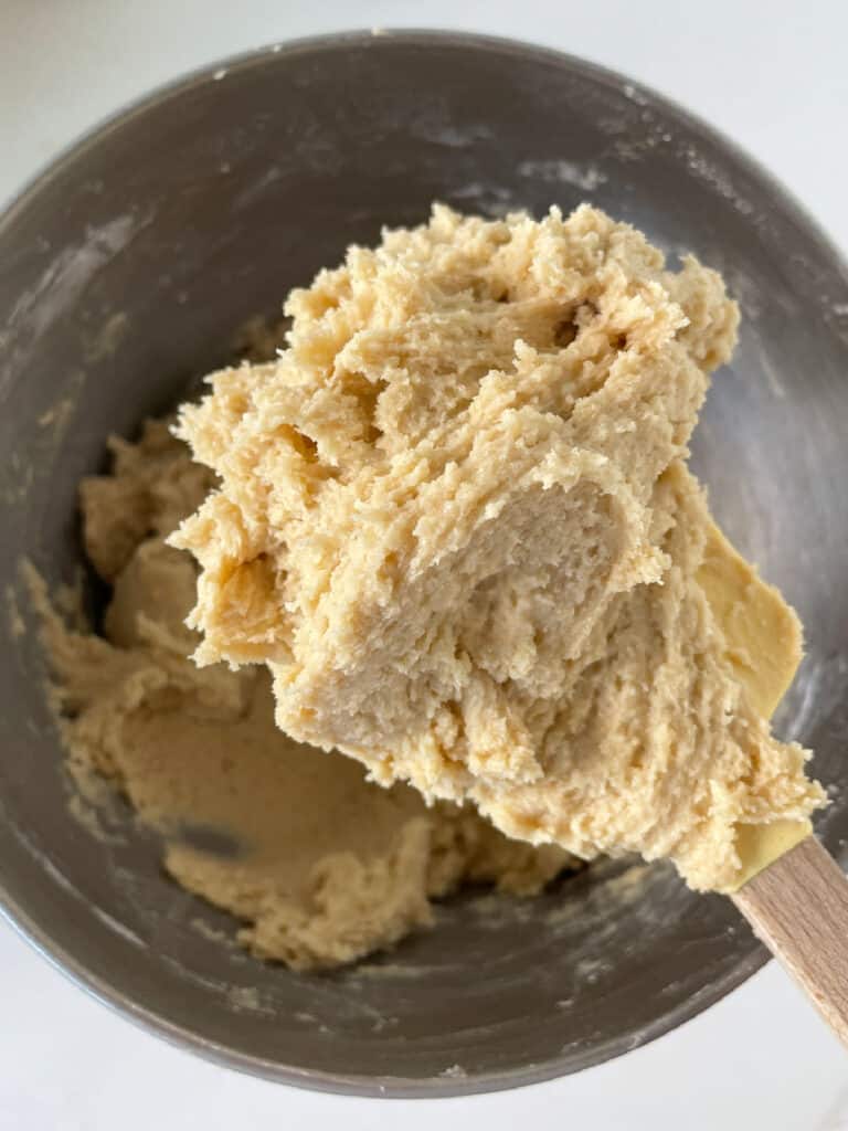 Spatula with cookie batter over a metal bowl.