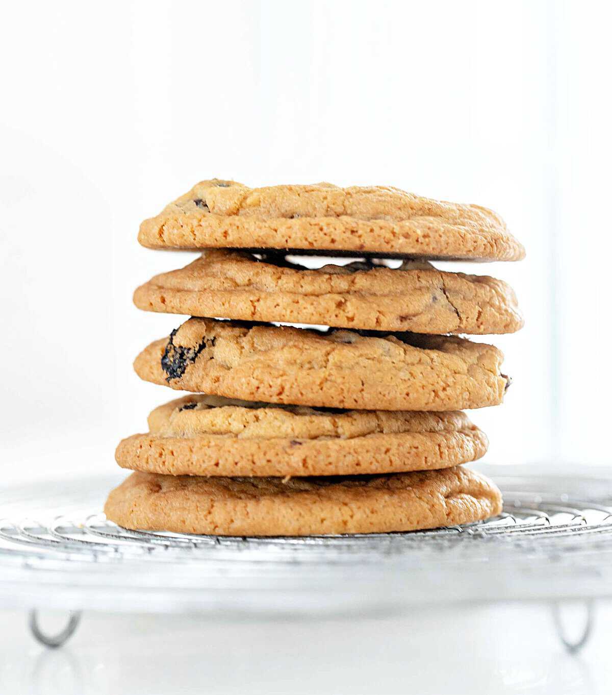 Wire rack with stack of raisin chip cookies. White background.