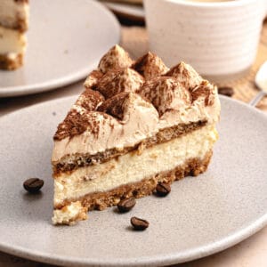 Slice of tiramisu cheesecake on a light gray plate. Coffee beans and coffee cup.