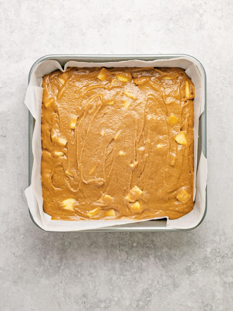 Light gray surface with lined metal square pan and applesauce crumb cake batter.