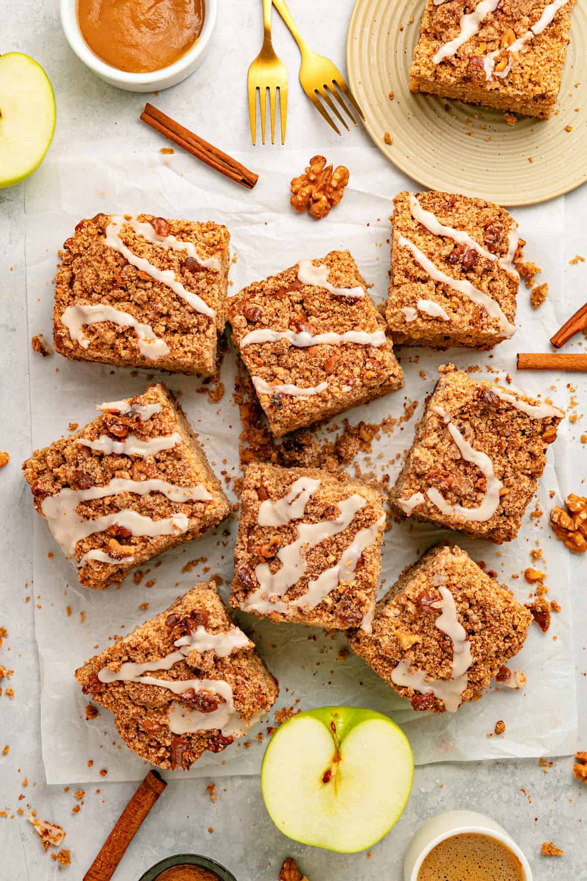 apple coffee cake Glazed pieces of applesauce coffee cake with crumble on a white paper. Apple pieces, cinnamon sticks, applesauce.
