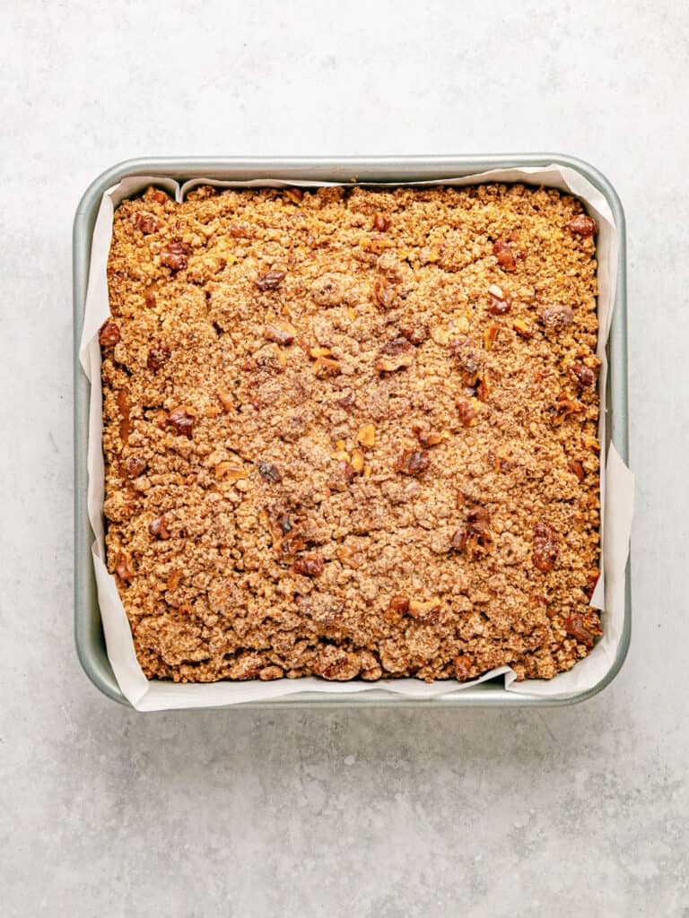 Lined metal square pan with crumb applesauce cake. Light gray surface.