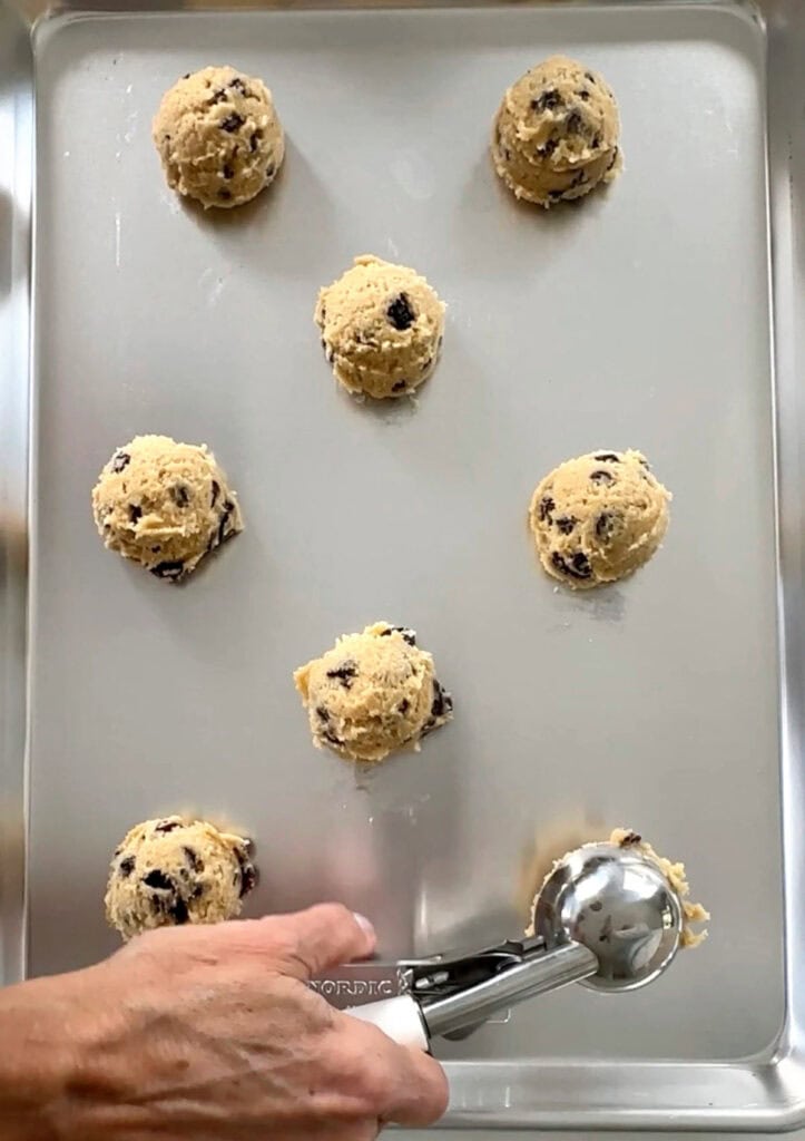 Scooping chocolate chip cookie dough balls on a metal cookie sheet. Top view.