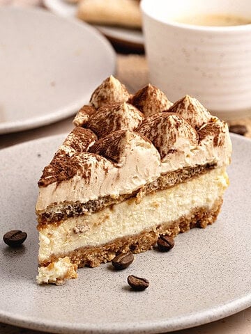 Light gray plate with slice of tiramisu serving. White coffee cup and plate in the background.