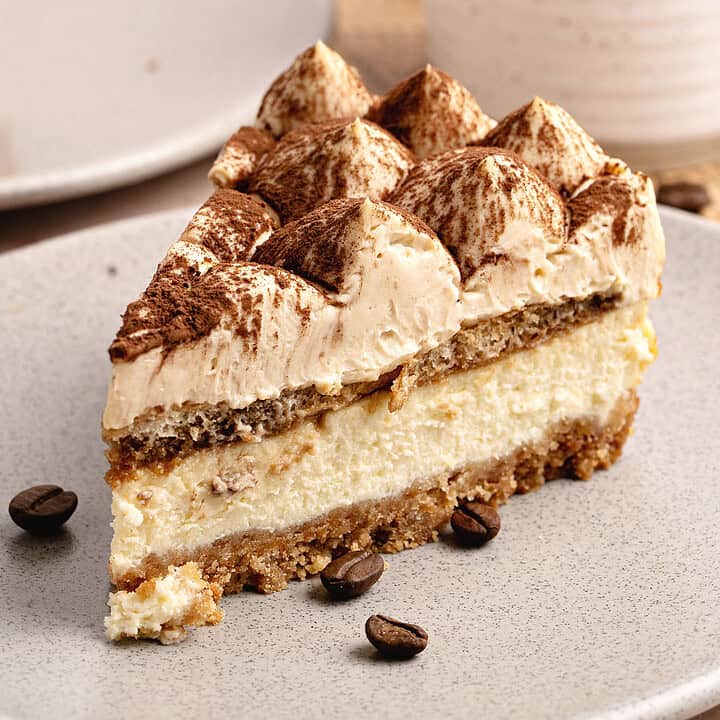 Light gray plate with slice of tiramisu serving. White coffee cup and plate in the background.