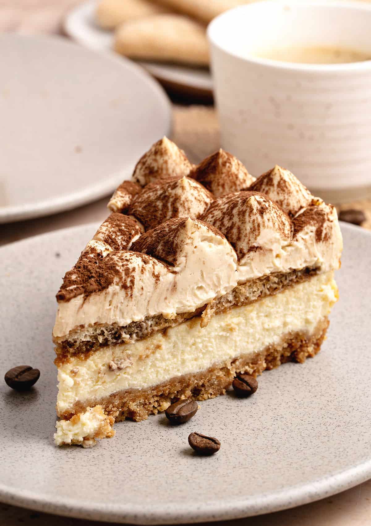 Light gray plate with slice of tiramisu serving. White coffee cup and plate in the background.