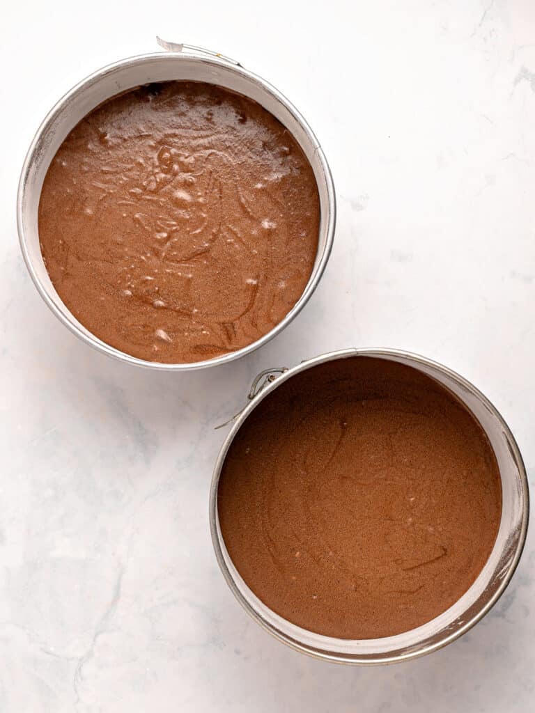 Two round metal cake pans with chocolate cake batter. White background.