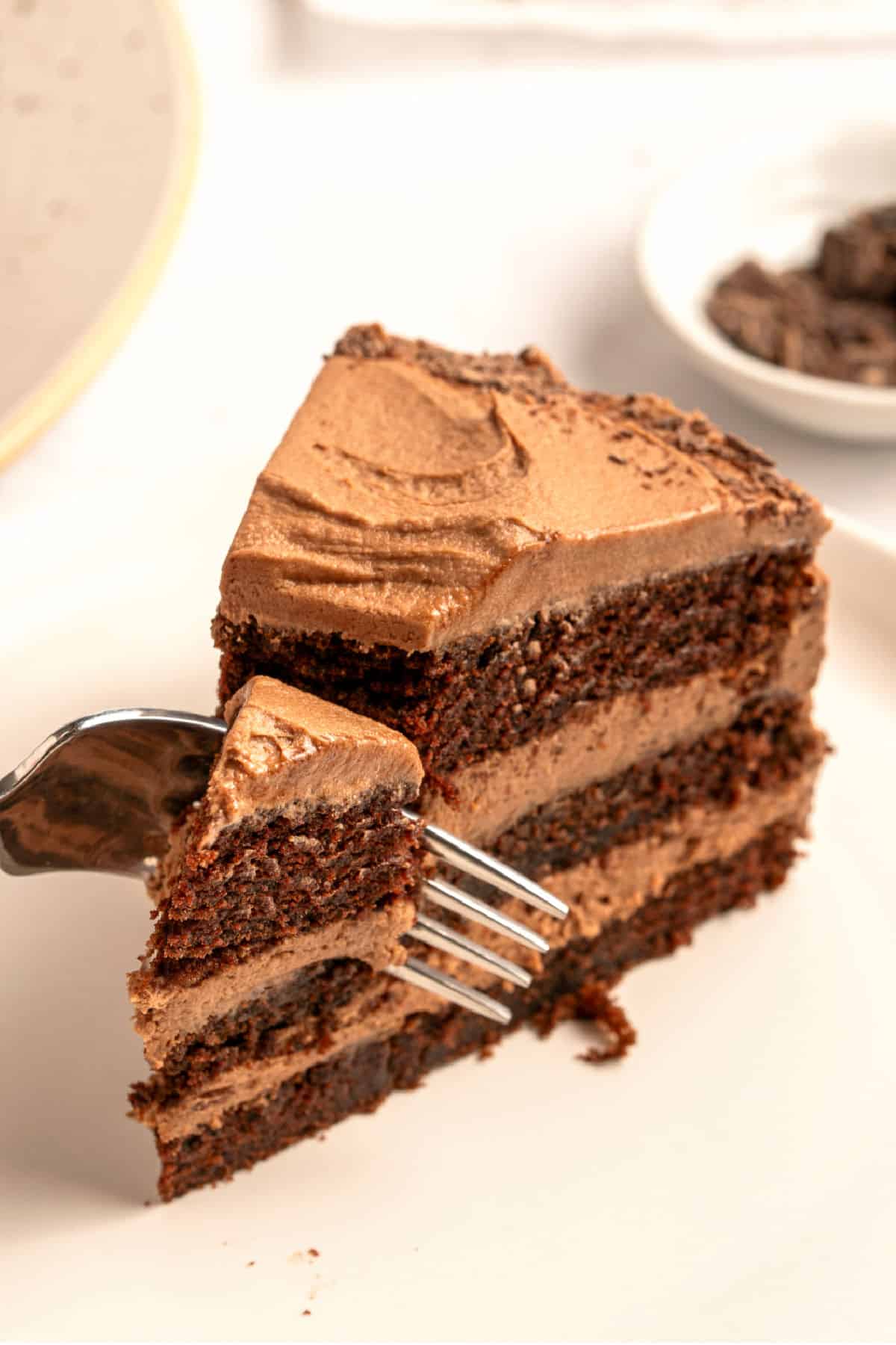 Forking a slice of old-fashioned frosted and filled chocolate cake. White plate and surface.