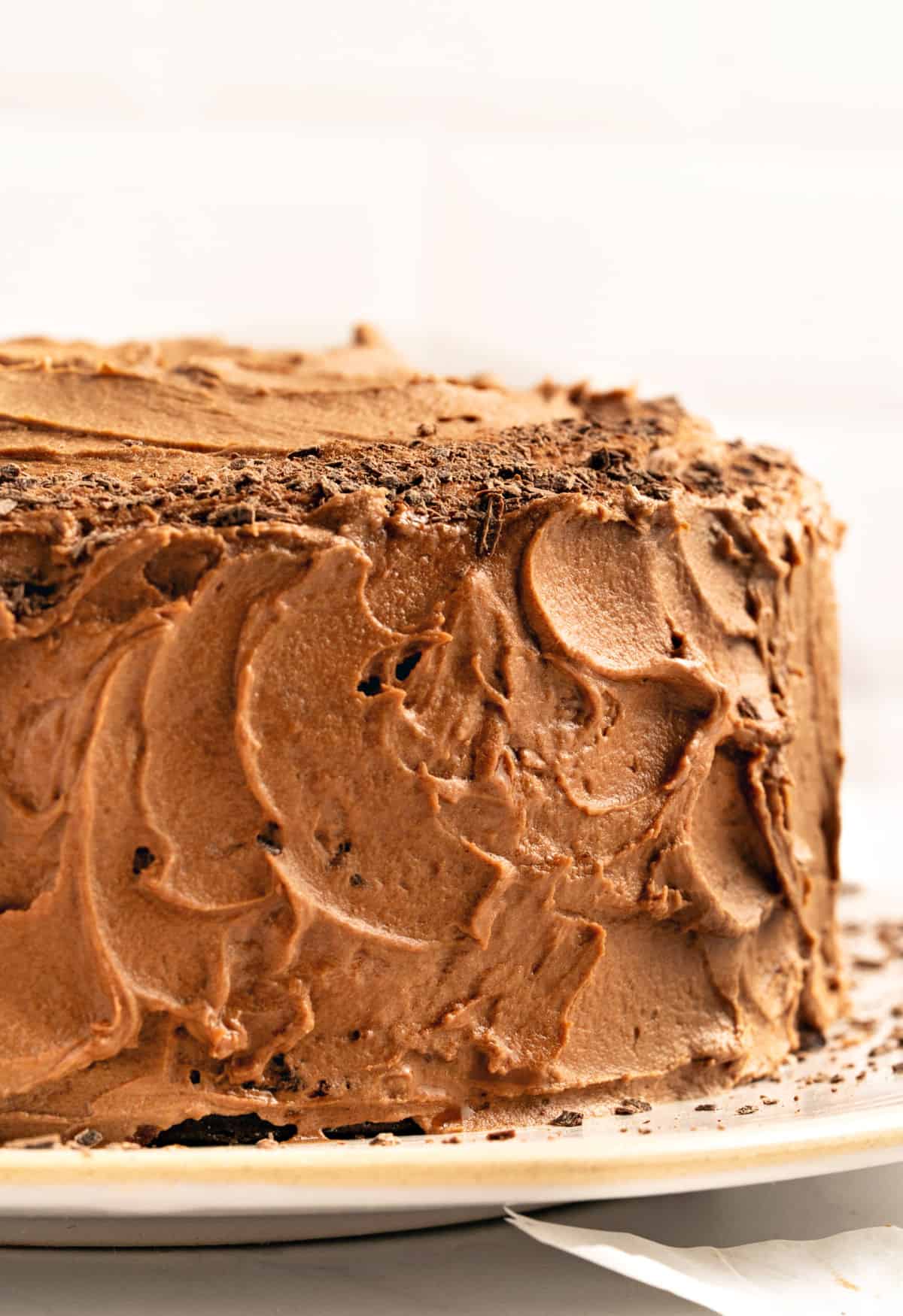 Partial view of tall chocolate frosted cake on a whitish plate and background.