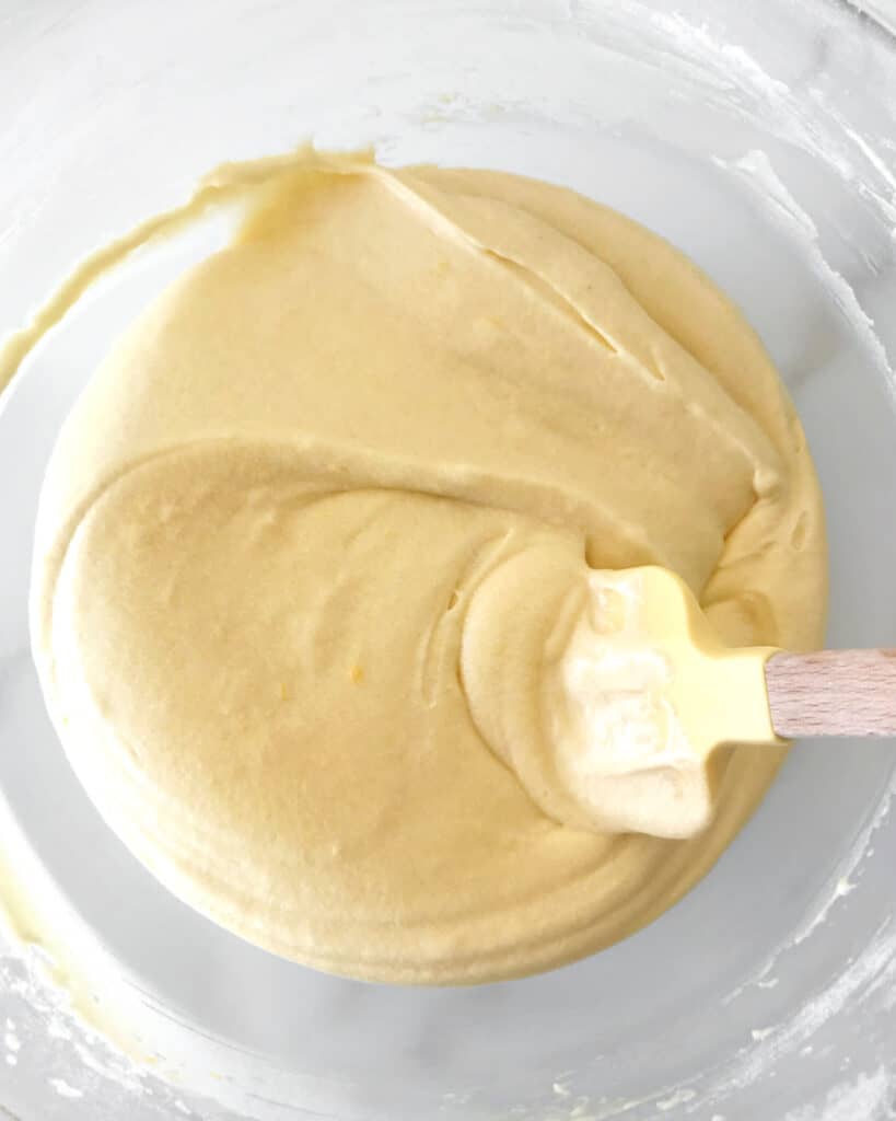 Yellow spatula with lemon cake batter in a glass bowl.