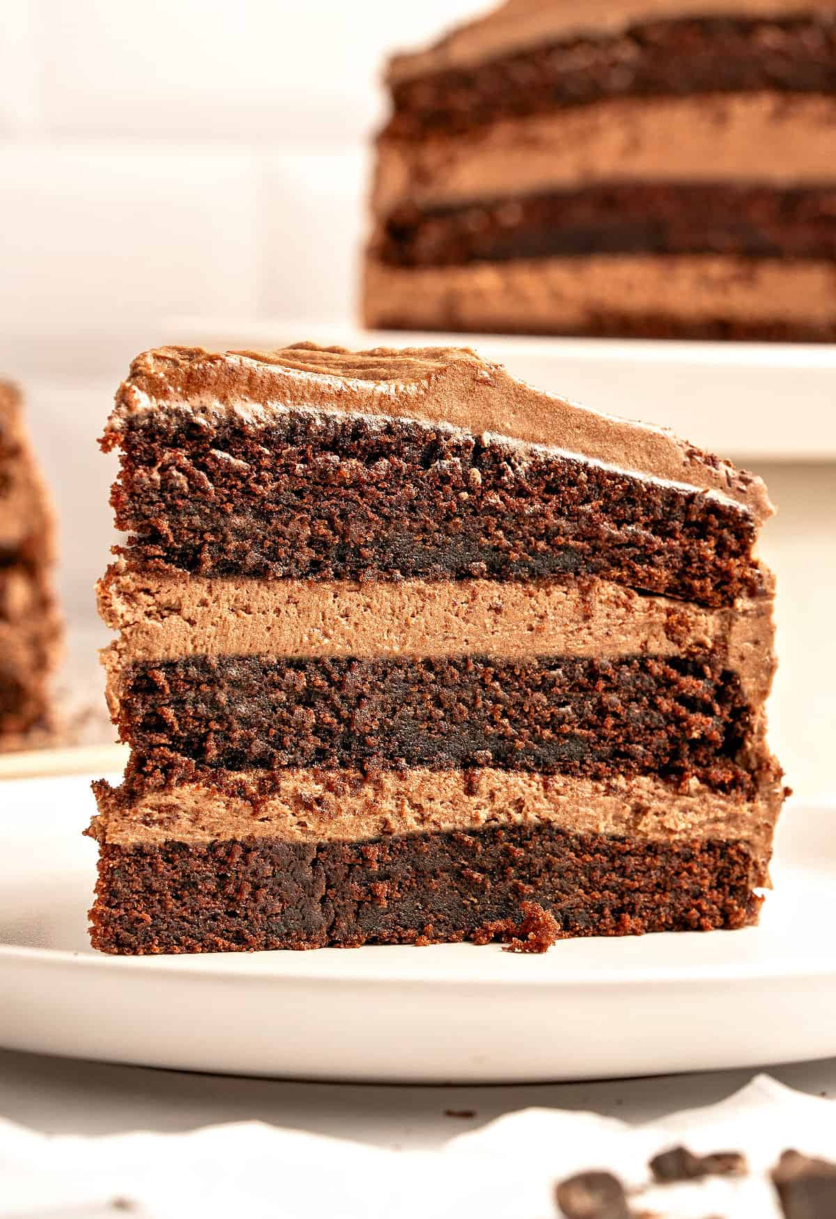 White plates with single slices of filled and frosted chocolate cake.