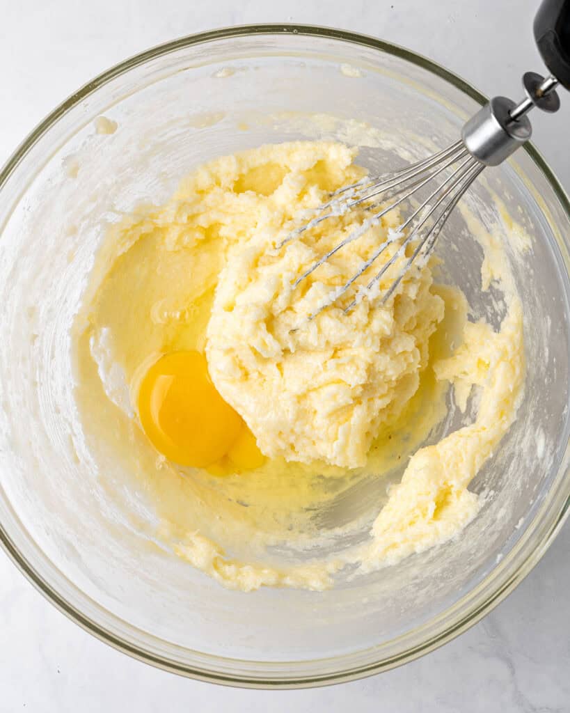 Glass bowl with creamed butter, sugar and whole egg. Whisk attachment. Gray background.
