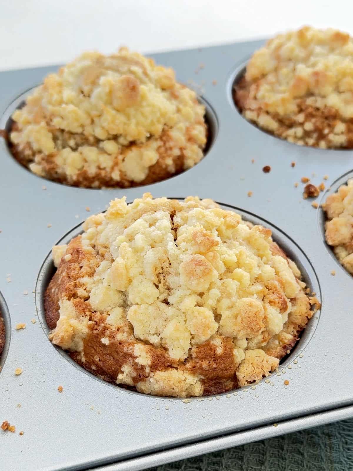 Metal jumbo muffin tin with baked apple muffins with crumble topping.