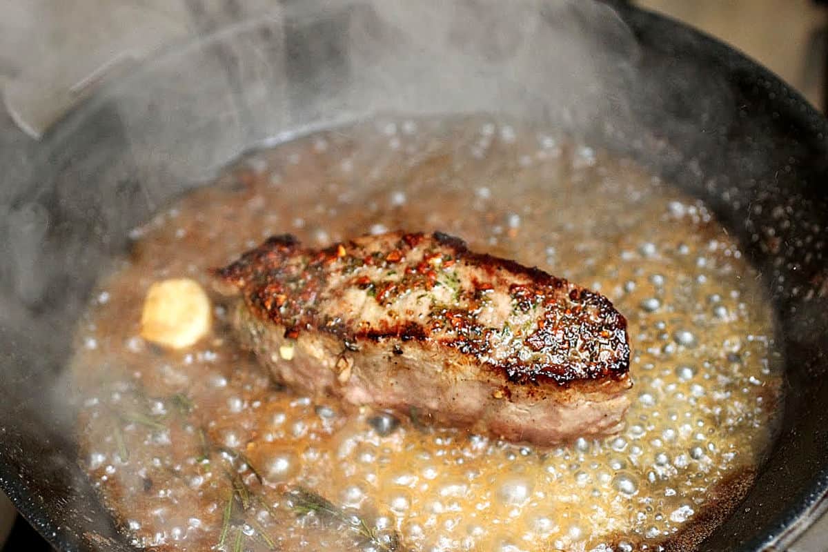 Pan cooking a rosemary garlic sirloin steak. Dark pan, sizzling wine sauce.
