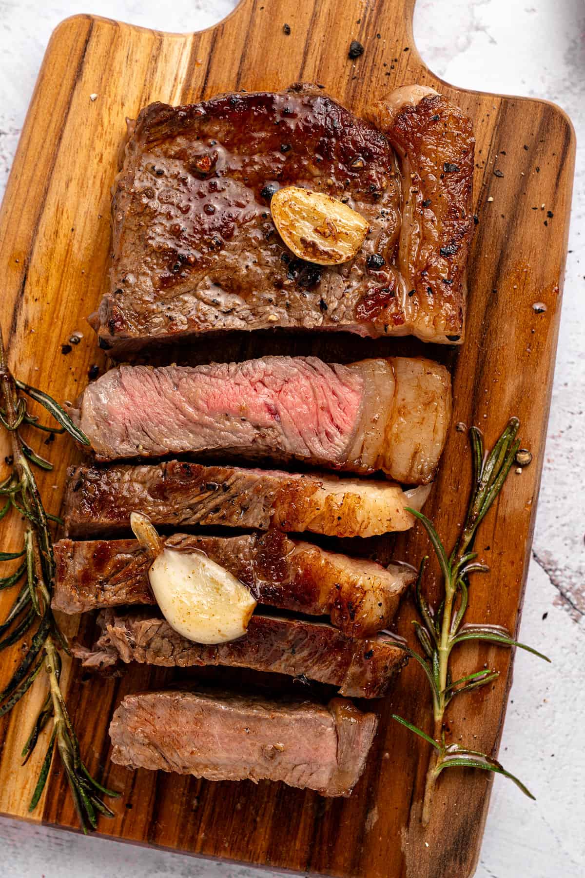 Sliced, medium juicy sirloin rosemary steak with garlic on a wooden board. 