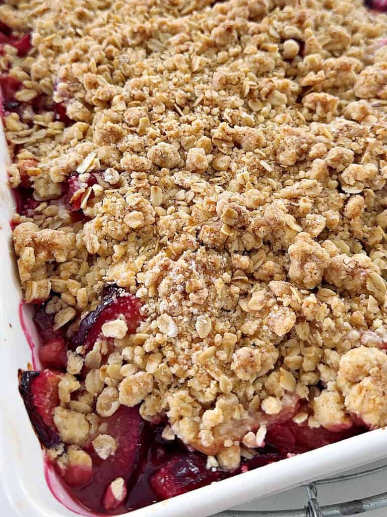 Baked plum crumble with oats in a white baking dish. Partial view.