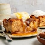 Maple and whipped cream-topped bread pudding servings on beige plates. Light gray background.