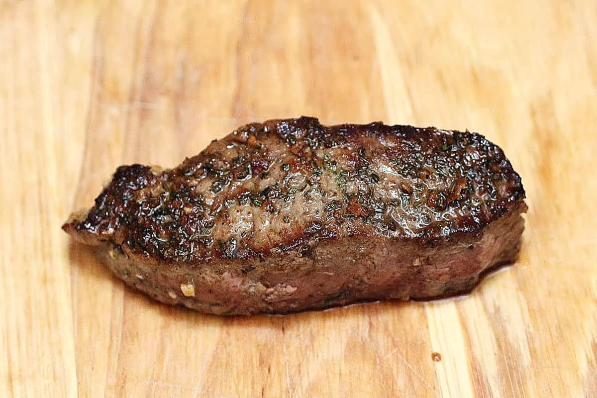 Seared rosemary garlic steak resting on a wooden board.
