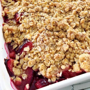 Close up baked plum crumble with oats in a white baking dish. Partial view.