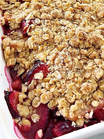 Close up baked plum crumble with oats in a white baking dish. Partial view.