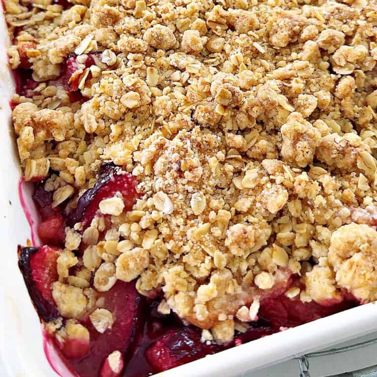 Close up baked plum crumble with oats in a white baking dish. Partial view.