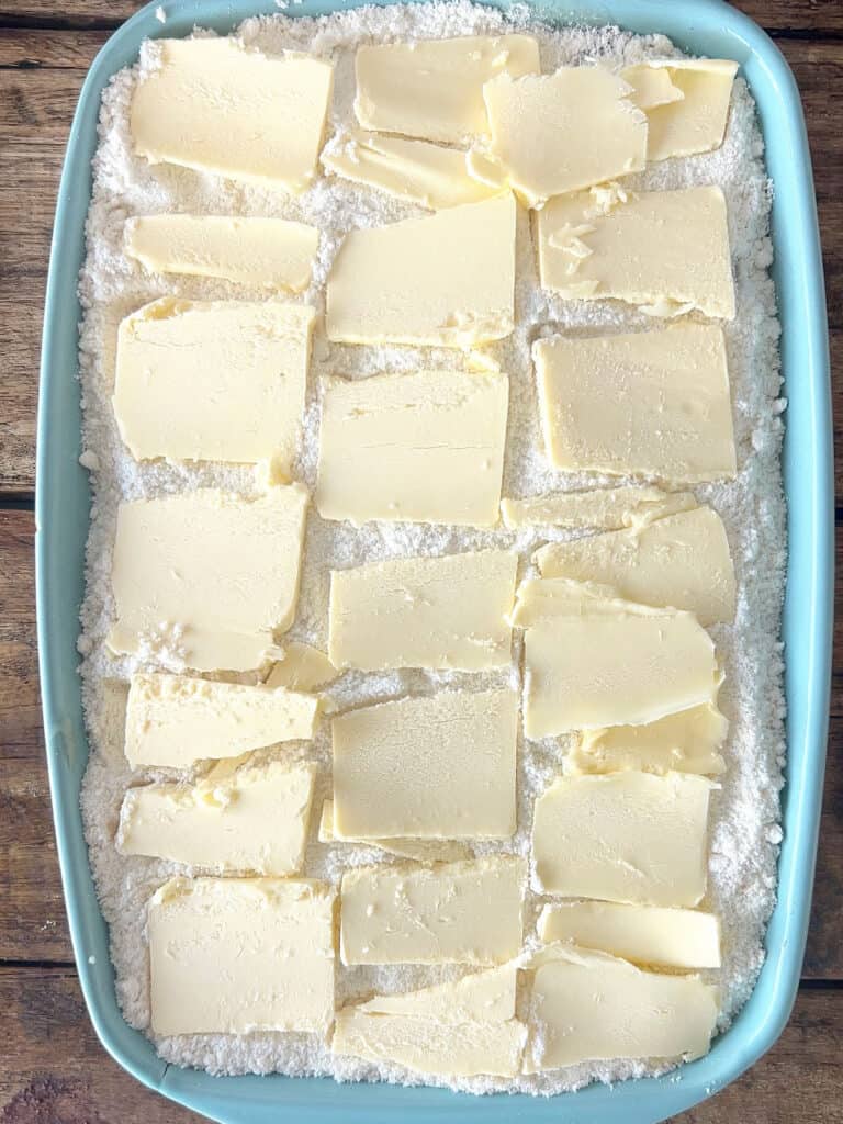 Butter slices on top of cake mix and apple pie filling. Blue baking dish.