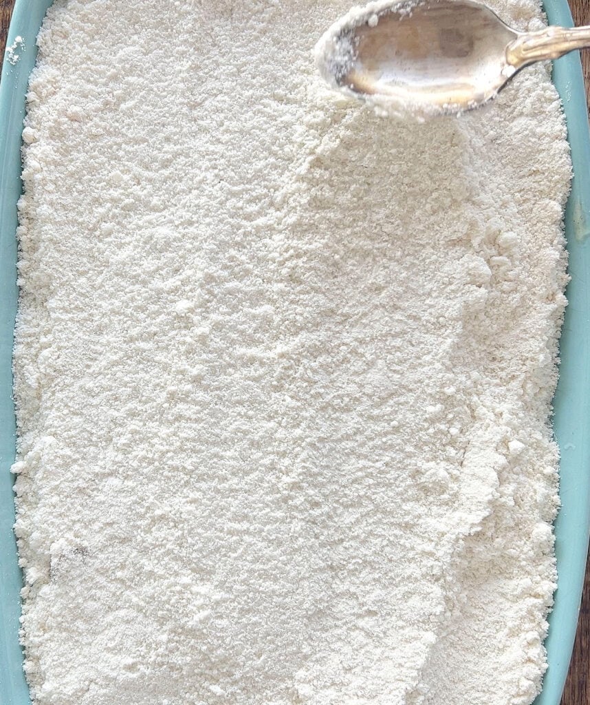 Smoothing cake mix topping for apple dump cake with a spoon.