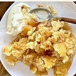 Serving of classic apple dump cake. White plate. Text overlay.
