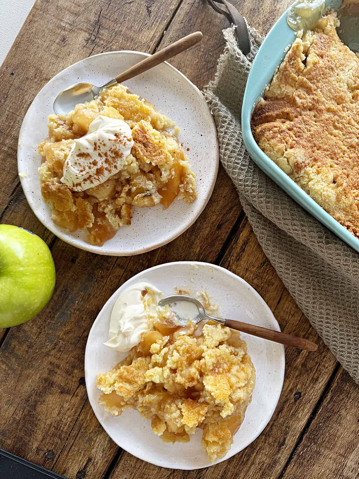 Wooden surface with servings of vintage apple dump cake on white plates.