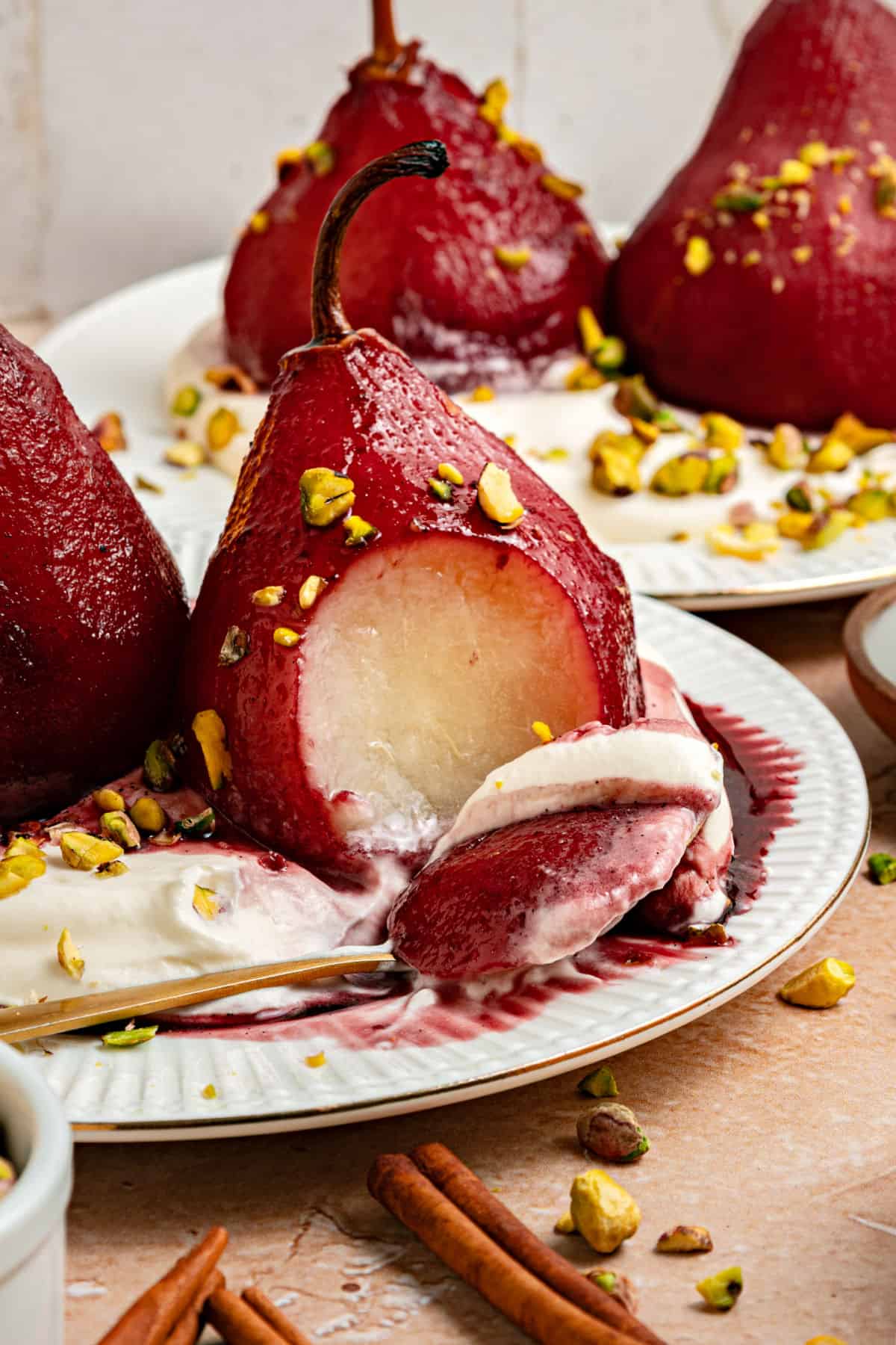 White plates with red wine poached pears. One is half eaten. Chopped pistachios, whipped cream.