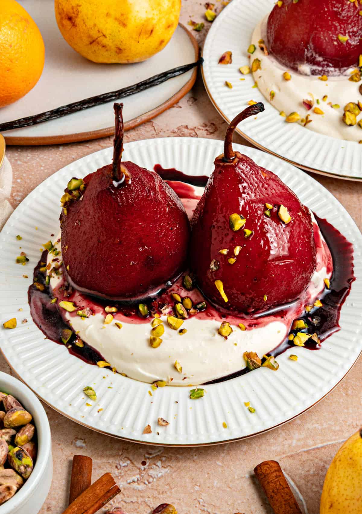 Two red wine pears over whipped cream and wine syrup on a white plate. Chopped pistachios.