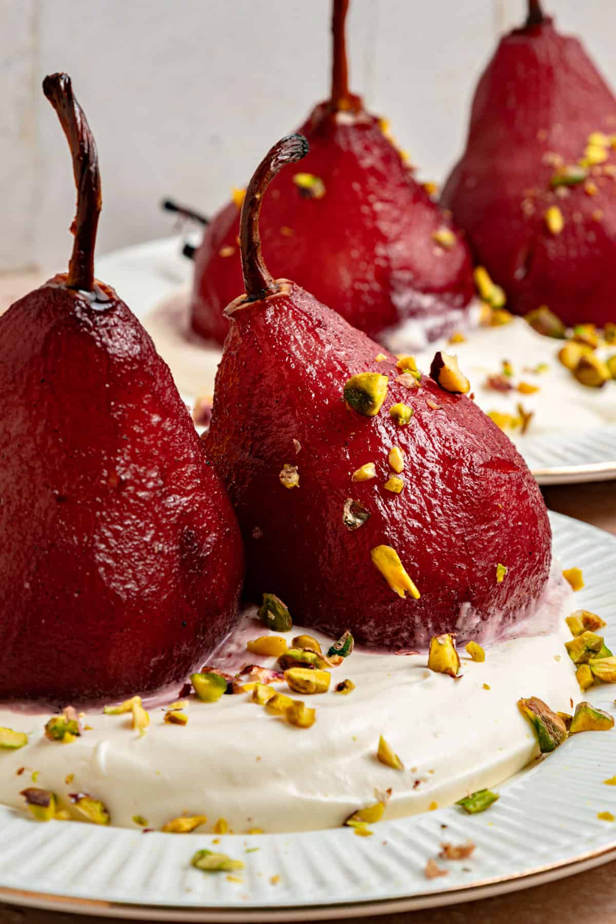 Red wine poached pears with whipped cream and pistachios on white plates.