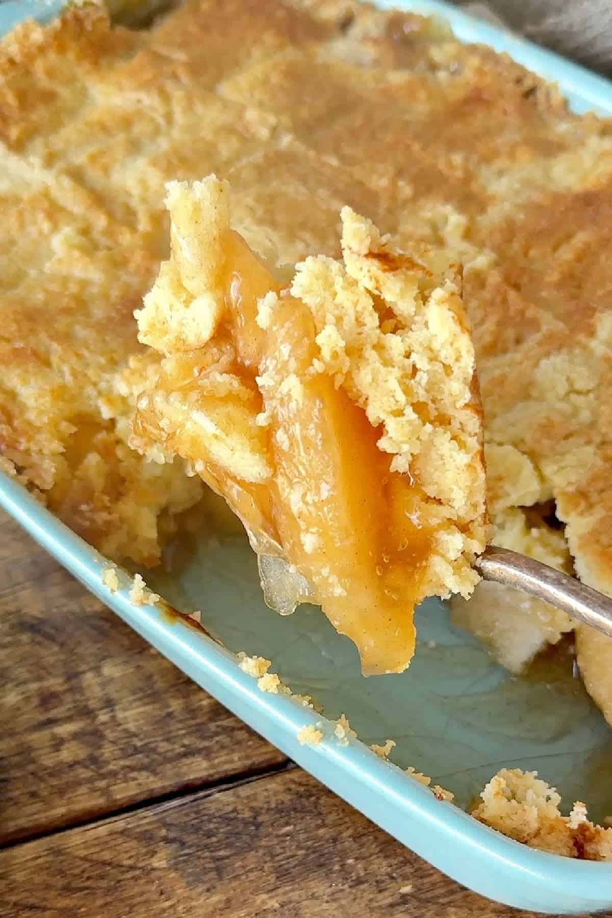 Lifting apple dump cake from a blue dish with a silver spoon.