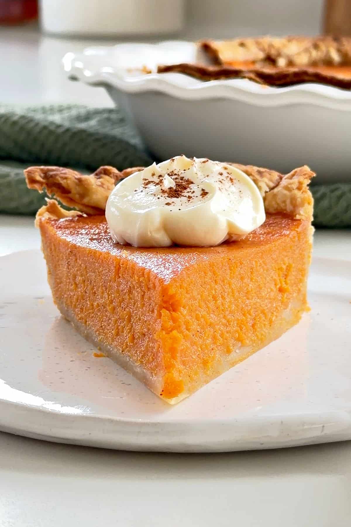 Font view of cream-topped classic sweet potato pie on a white plate.