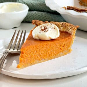 Close up slice of vintage sweet potato pie with dollop of cream and cinnamon. White plate and silver fork.