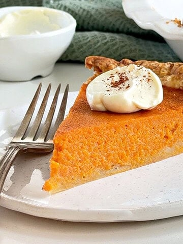 Close up slice of vintage sweet potato pie with dollop of cream and cinnamon. White plate and silver fork.