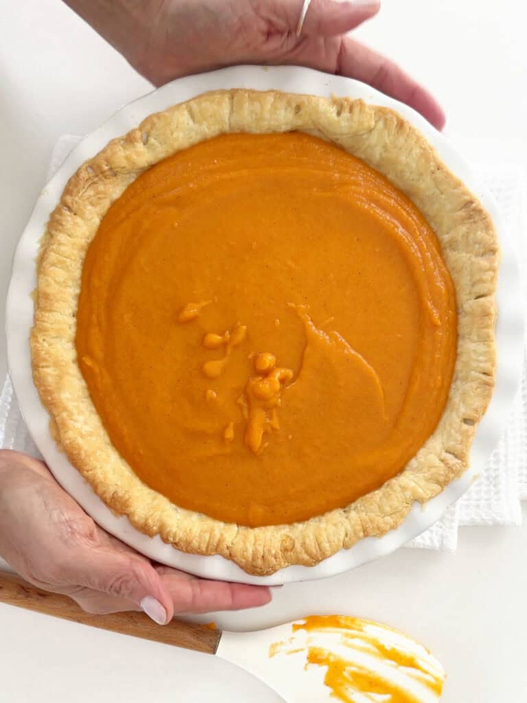 Unbaked sweet potato pie in a white dish. Hands holding it. Top view.