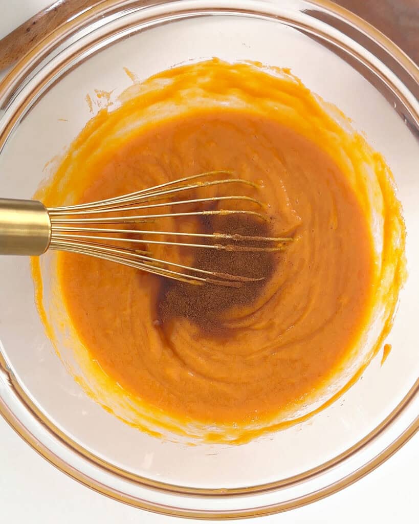 Whisking spiced grandma-style sweet potato pie filling in a glass bowl. Gold whisk.